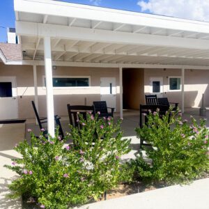A lush green shrub with pink flowers in front of a covered outdoor seating area at Harbor Care Found.