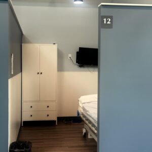 A hospital room with a bed, wardrobe, and wall-mounted TV in a healthcare facility.